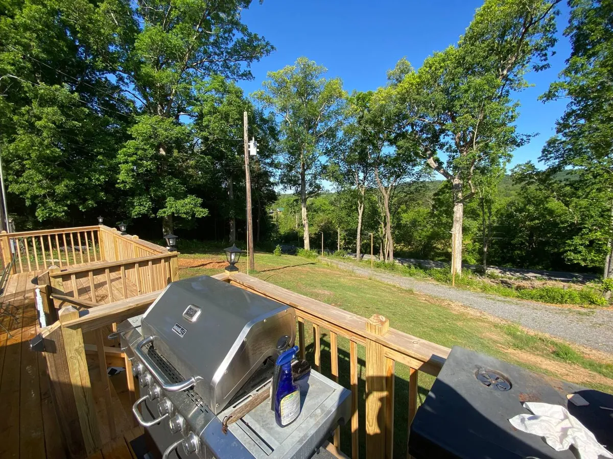 A view of the cottage’s exterior showing the grill area, deck, and open tree-lined space. The scene suggests a welcoming entry point for riders, with plenty of room for outdoor equipment and easy access to the natural surroundings, reinforcing the property as a basecamp for outdoor pursuits.