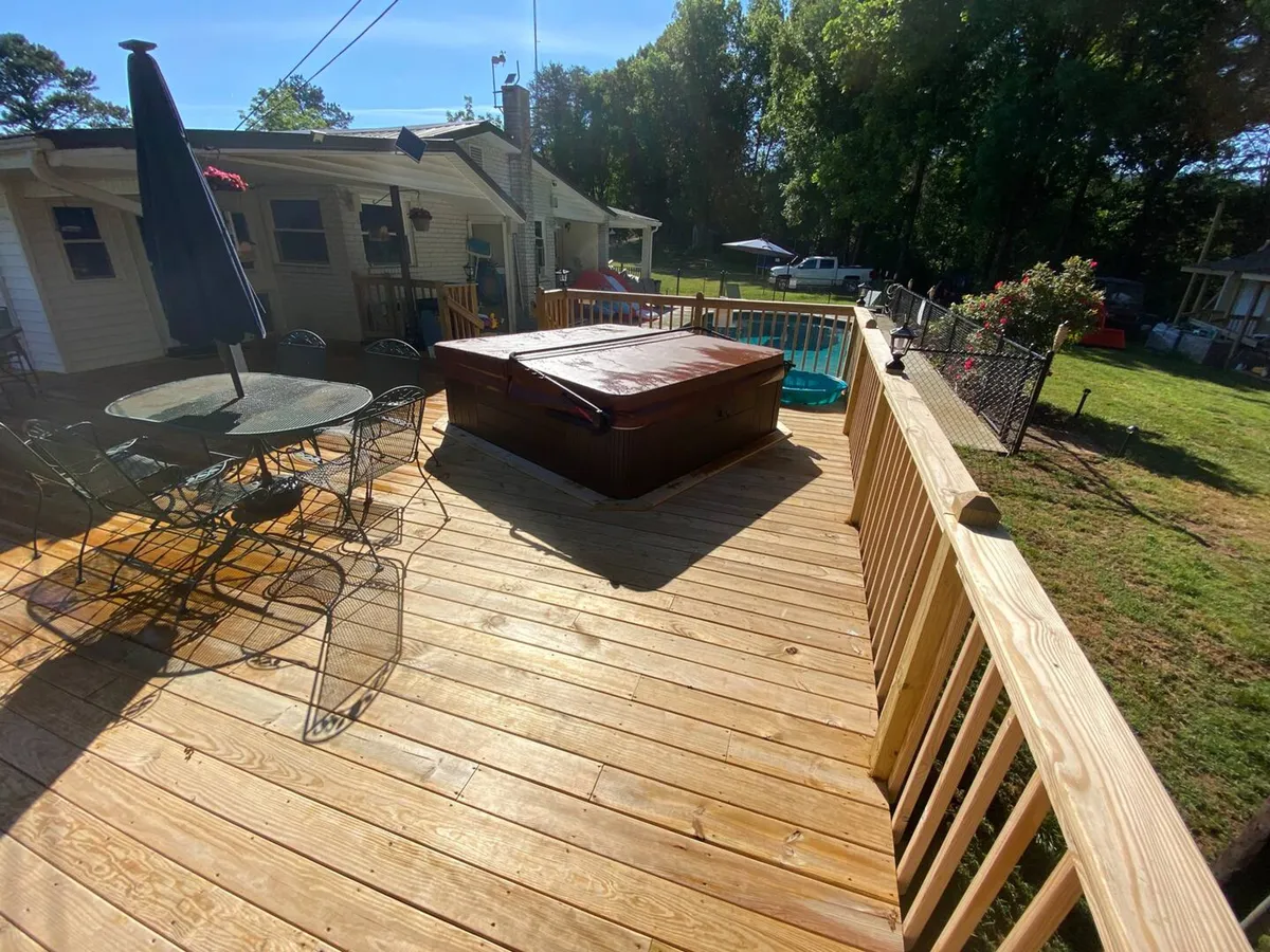 A tranquil scene on the deck, featuring a bubbling hot tub with sunset views, an elegant outdoor dining table, charming deck railing, and lush garden space beyond. The atmosphere is inviting and serene, perfect for unwinding in the hot tub or enjoying meals al fresco.