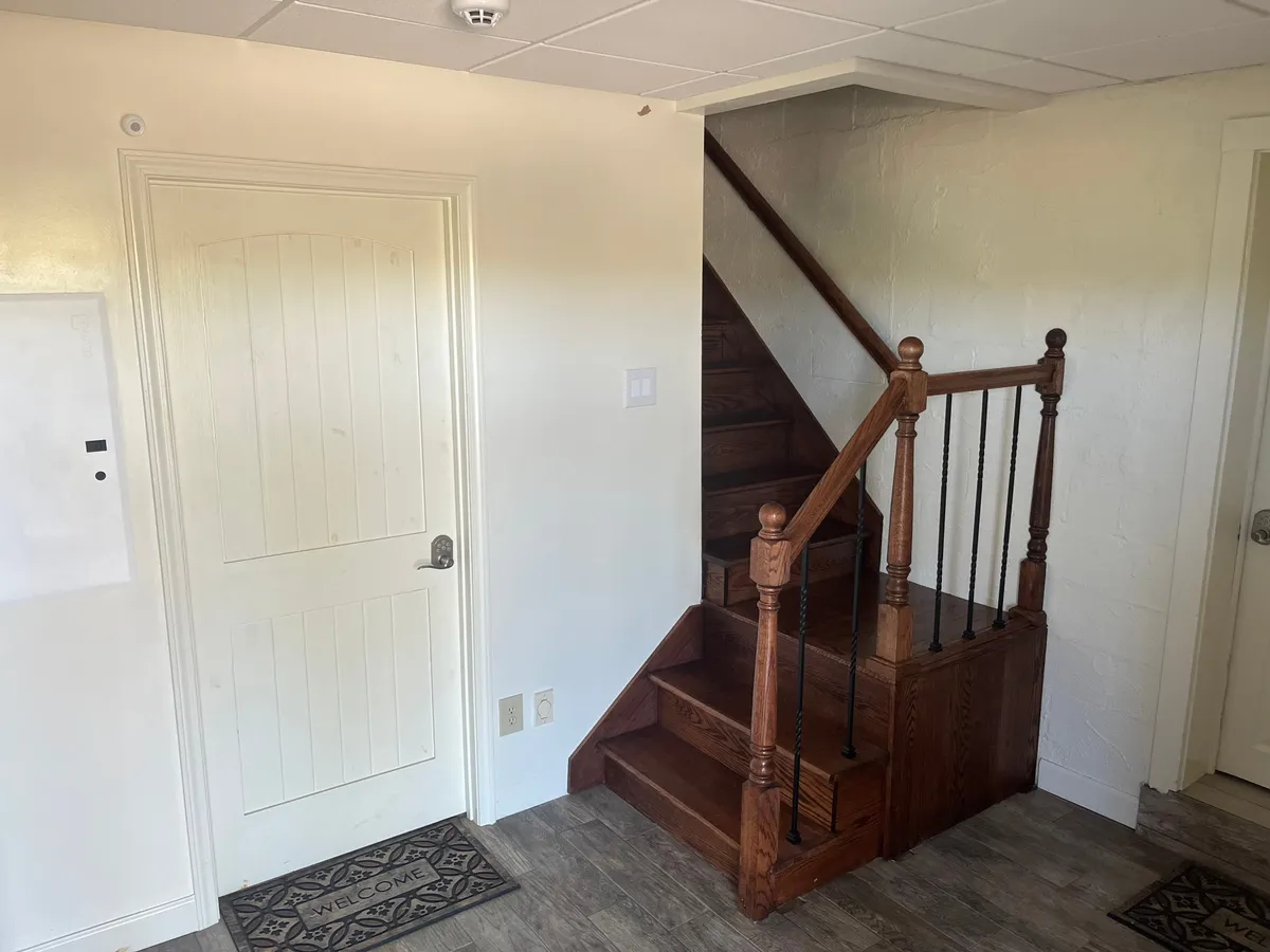 An inviting entryway with a staircase, entry door, and a welcoming mat, bathed in soft natural light. The setting is both practical and charming, evoking the transition from the outside world to a peaceful interior retreat.