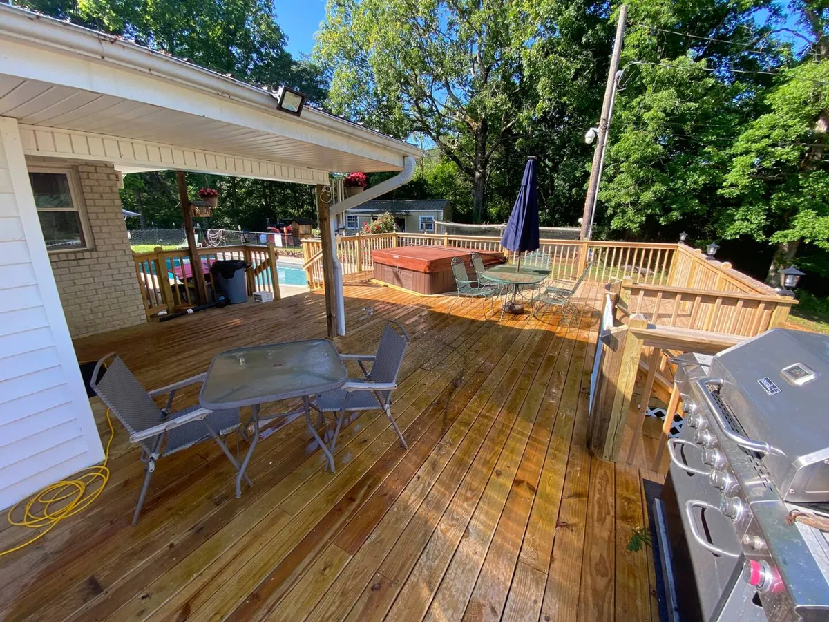 This image captures the cottage's exterior deck with a hot tub, grill, and dining table, set against the backdrop of a relaxed and social outdoor environment. The spacious deck hints at ample room for parking motorcycles or storing gear, while the privacy and comfort of the setting reinforce the cottage’s role as a relaxing retreat after a day of adventure.