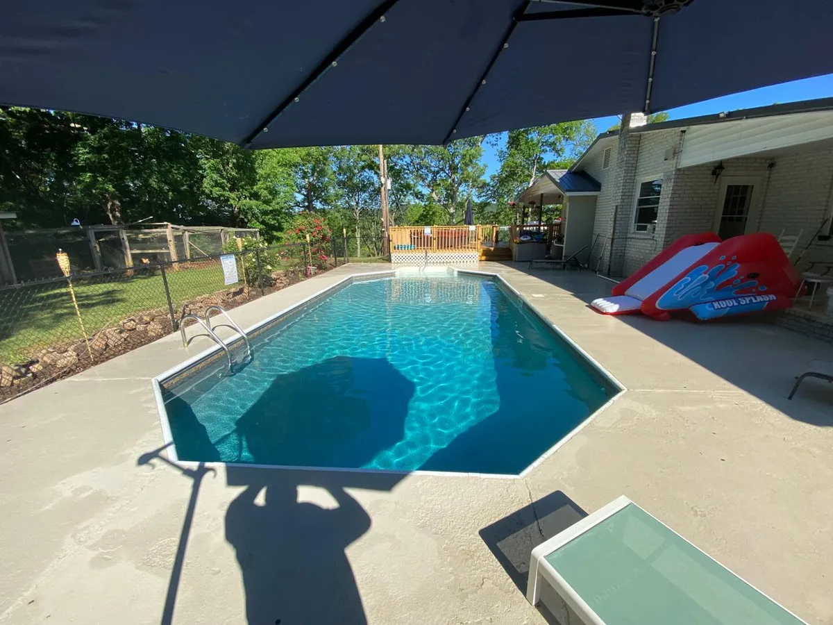 A vibrant exterior scene featuring a sparkling swimming pool with a fun pool slide, surrounded by ample outdoor seating, lush greenery, and a fenced area that ensures privacy. The space is set up for relaxing, sunbathing, and gathering, exuding a relaxed and inviting resort-style vibe.